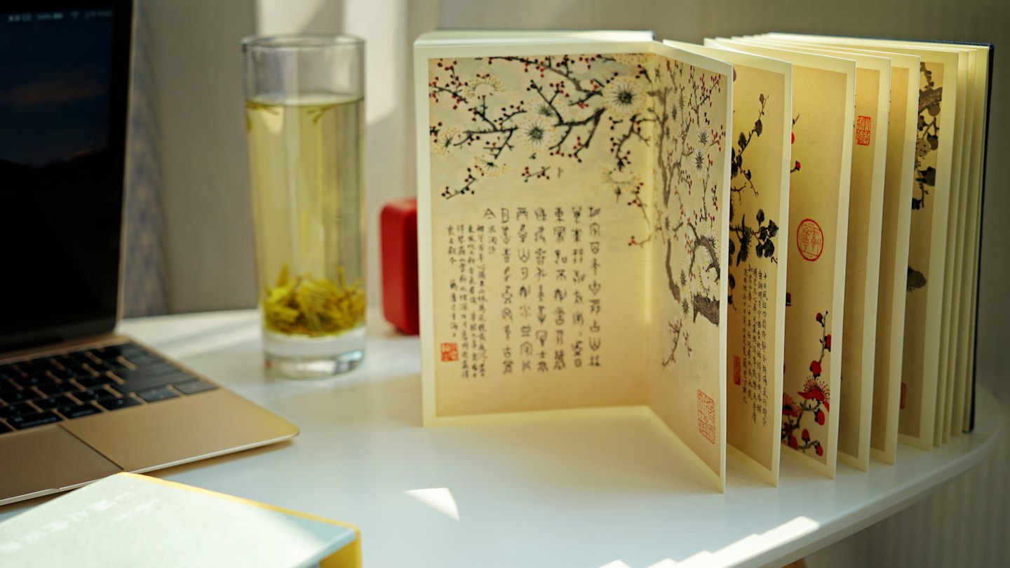 Home Un libro aperto di dipinti a inchiostro accanto a un laptop e a una tazza di tè.